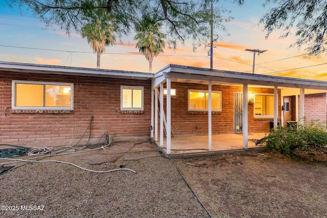 back of property at dusk featuring brick siding and a patio