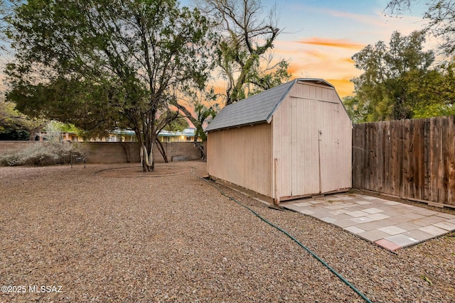 outdoor structure at dusk featuring a storage shed, a fenced backyard, and an outdoor structure