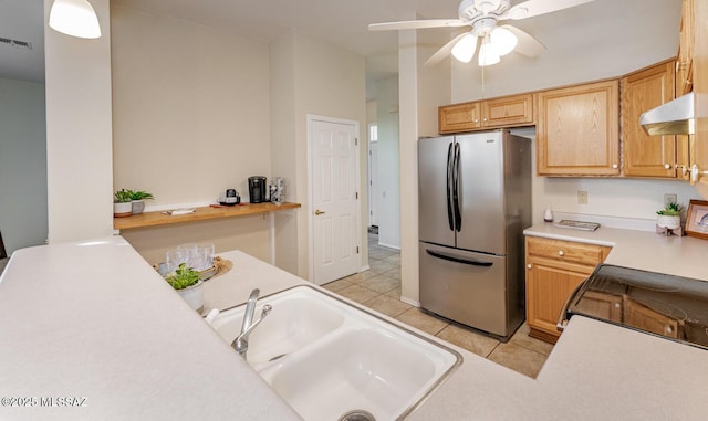 kitchen with light tile patterned floors, under cabinet range hood, a sink, light countertops, and freestanding refrigerator