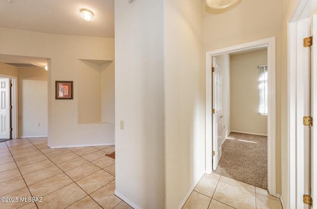 corridor with light carpet, light tile patterned floors, and baseboards