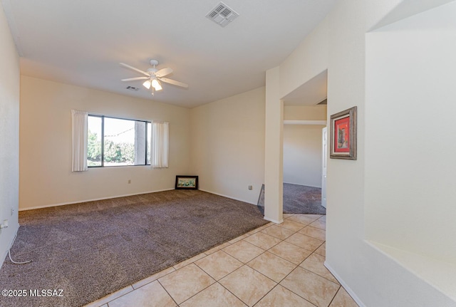 empty room featuring light tile patterned floors, visible vents, a ceiling fan, and light colored carpet