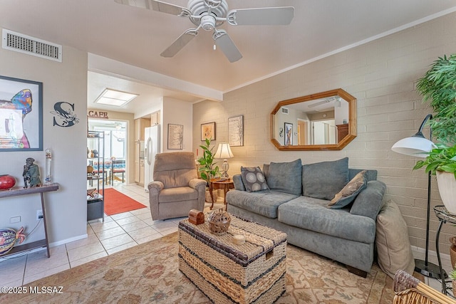 living area with light tile patterned floors, visible vents, baseboards, brick wall, and ceiling fan