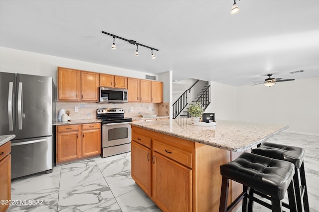 kitchen with light stone countertops, marble finish floor, tasteful backsplash, and stainless steel appliances