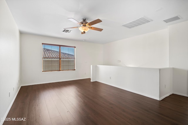 empty room featuring dark wood-type flooring, visible vents, and a ceiling fan