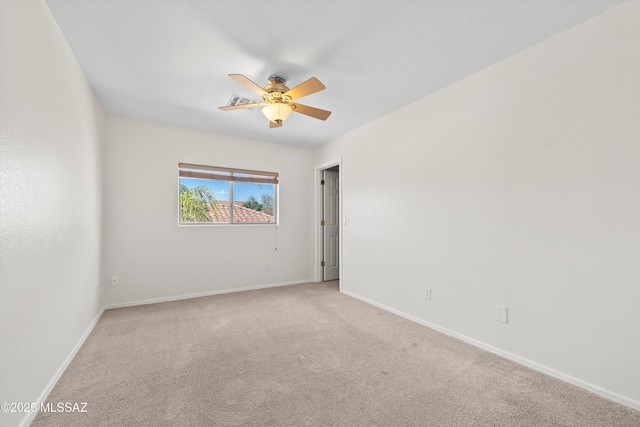 spare room featuring light carpet, a ceiling fan, and baseboards