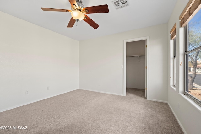 unfurnished bedroom featuring light colored carpet, visible vents, a spacious closet, ceiling fan, and baseboards