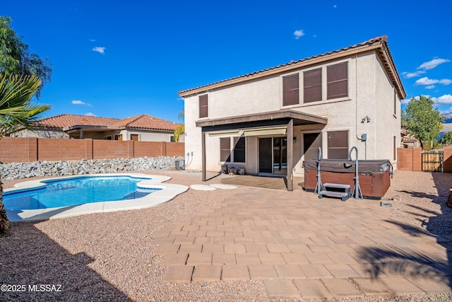 back of property featuring a hot tub, a fenced in pool, a fenced backyard, a patio area, and stucco siding