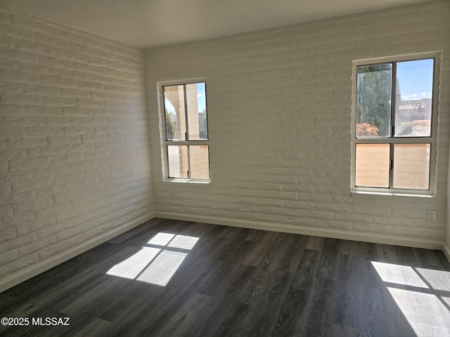 unfurnished room with baseboards, brick wall, and dark wood-style flooring