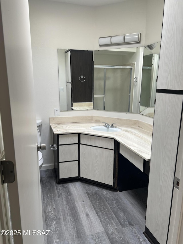 full bath with toilet, wood finished floors, a shower stall, baseboards, and vanity