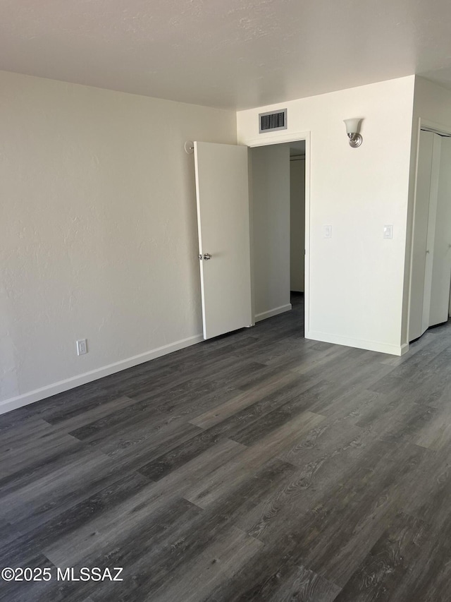 unfurnished room featuring visible vents, dark wood-type flooring, and baseboards