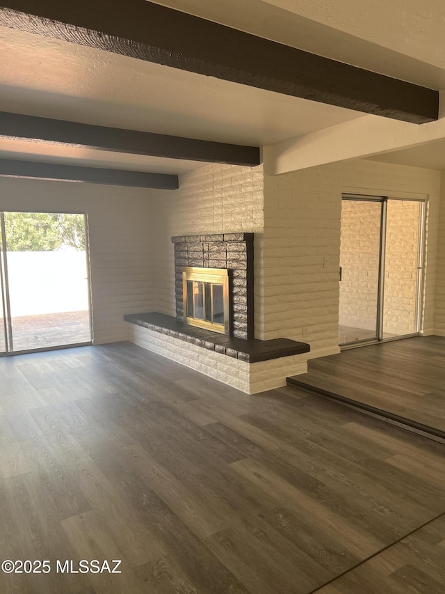 unfurnished living room featuring beam ceiling, brick wall, wood finished floors, and a fireplace