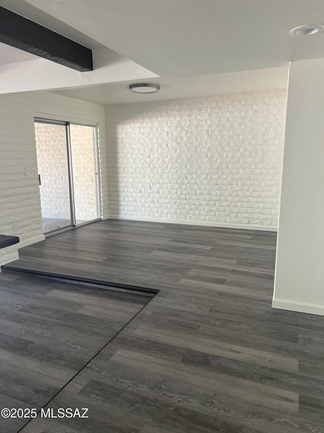 empty room featuring beam ceiling, brick wall, and wood finished floors