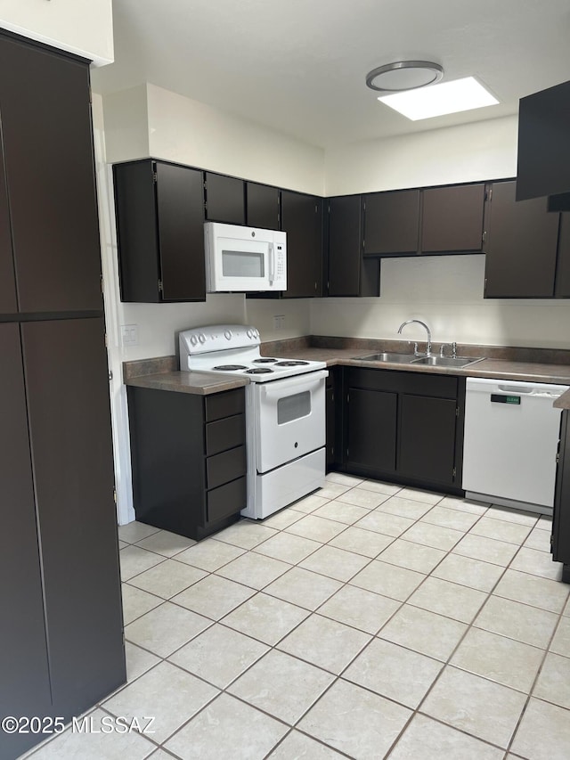 kitchen featuring light tile patterned floors, dark cabinets, white appliances, and a sink