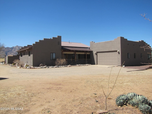 view of front facade with stucco siding, an attached garage, and dirt driveway