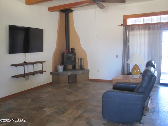 living room with beam ceiling, a wood stove, a ceiling fan, and baseboards