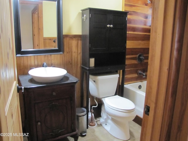 bathroom featuring a wainscoted wall, toilet, wooden walls, a bath, and vanity
