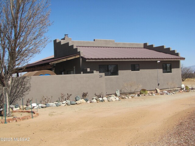 view of side of property featuring stucco siding, metal roof, fence, and a chimney