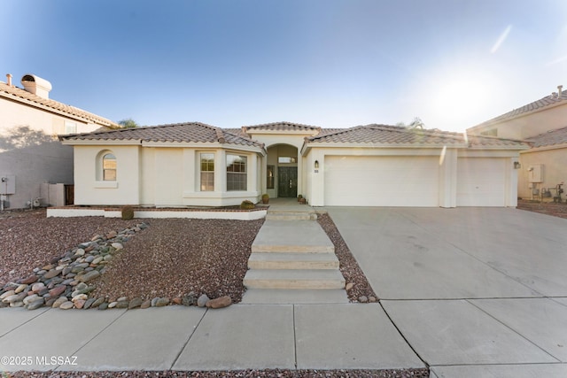 mediterranean / spanish home featuring concrete driveway, a tiled roof, a garage, and stucco siding