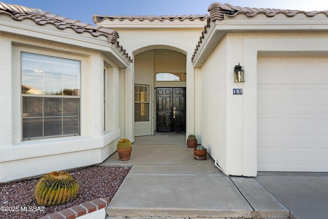 view of exterior entry featuring stucco siding, a tiled roof, and an attached garage