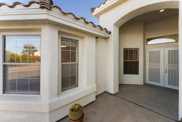 view of exterior entry with french doors, stucco siding, and a tiled roof