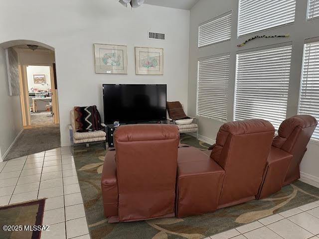 living room with visible vents, baseboards, light tile patterned floors, a high ceiling, and arched walkways