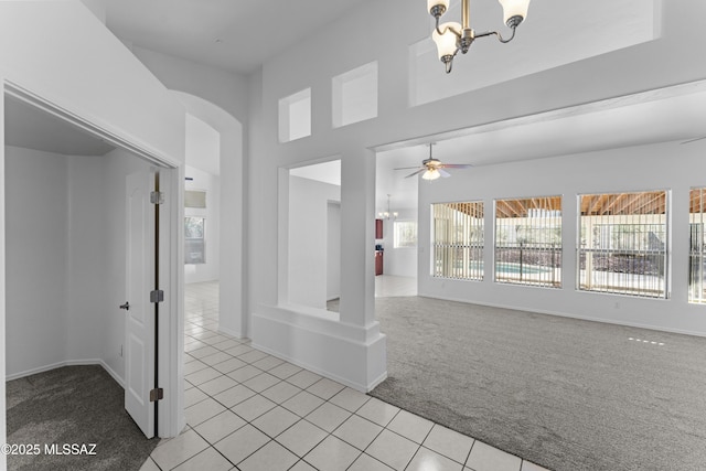 interior space featuring light tile patterned floors, baseboards, arched walkways, light carpet, and ceiling fan with notable chandelier