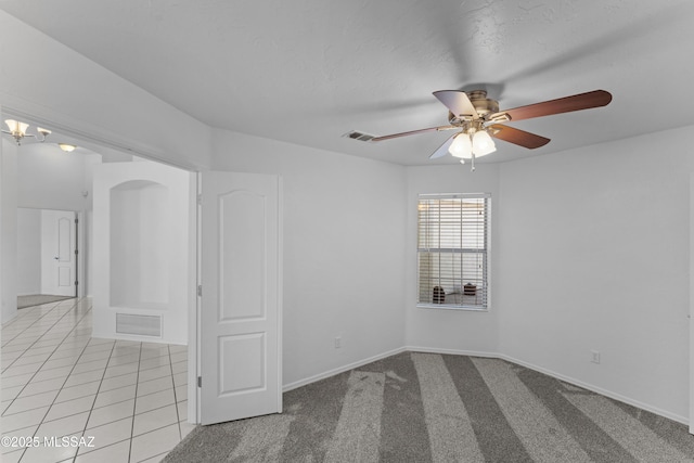 empty room featuring light tile patterned flooring, visible vents, ceiling fan with notable chandelier, and light carpet