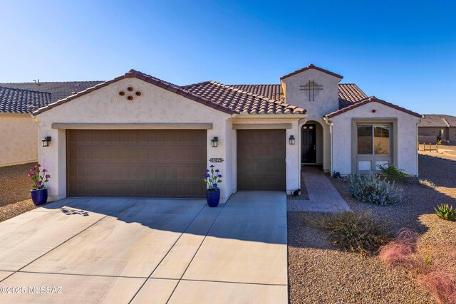 mediterranean / spanish home with a tiled roof, stucco siding, an attached garage, and concrete driveway