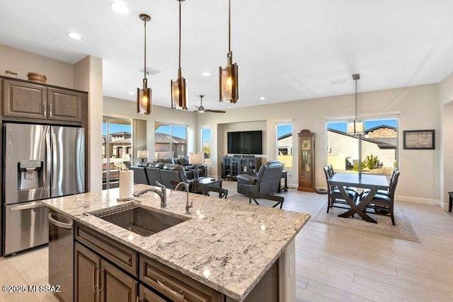 kitchen with a center island with sink, pendant lighting, light wood-type flooring, stainless steel appliances, and a sink