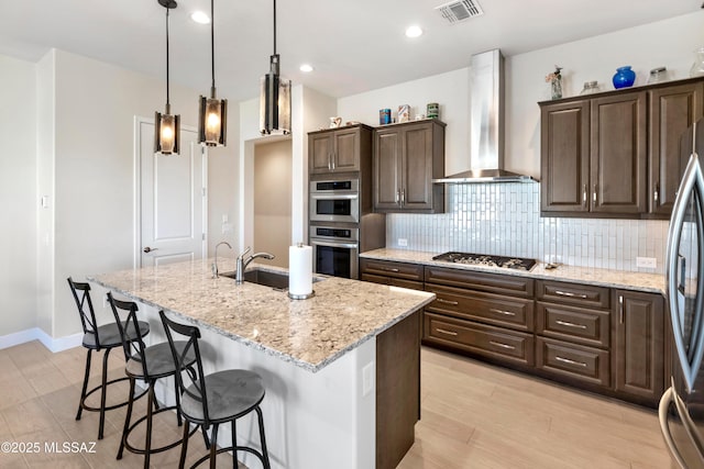 kitchen with visible vents, backsplash, appliances with stainless steel finishes, wall chimney exhaust hood, and a sink