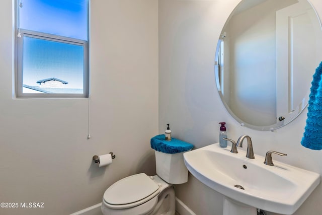 half bathroom featuring toilet, baseboards, and a sink