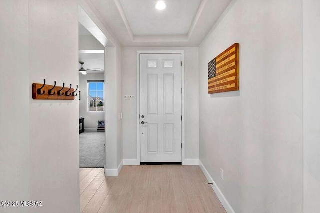 entryway with a raised ceiling, light wood-style floors, and baseboards