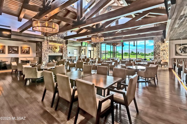 dining area featuring a chandelier, beam ceiling, a stone fireplace, and wood finished floors