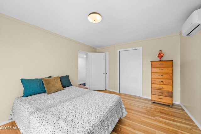 bedroom with ornamental molding, a wall mounted AC, a closet, light wood-style floors, and baseboards