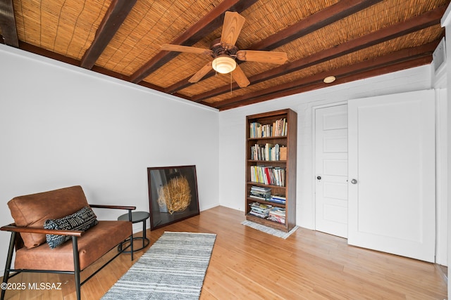 living area with beam ceiling, wood ceiling, wood finished floors, and a ceiling fan