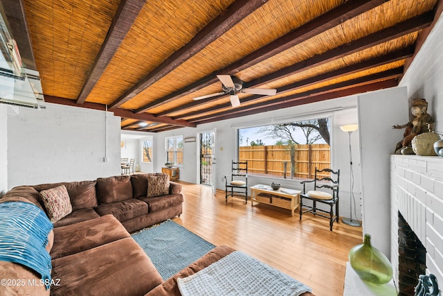 living room with beam ceiling, wood ceiling, wood finished floors, a brick fireplace, and ceiling fan