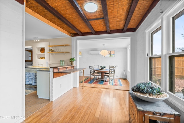 kitchen featuring beam ceiling, a wealth of natural light, a wall unit AC, and light wood finished floors