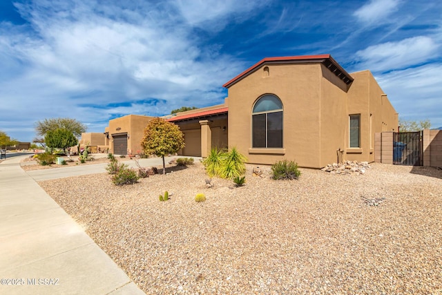 view of front facade with stucco siding, driveway, a gate, fence, and a garage