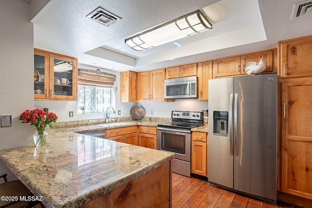 kitchen with visible vents, dark wood-style floors, stainless steel appliances, a peninsula, and a raised ceiling