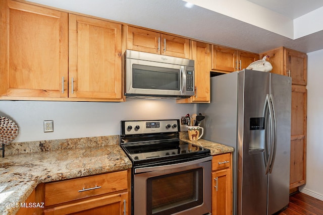 kitchen with brown cabinetry, dark wood finished floors, appliances with stainless steel finishes, and light stone countertops