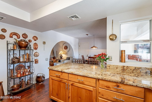 kitchen with dark wood-style floors, visible vents, arched walkways, and light stone counters