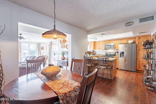 dining space featuring dark wood finished floors, ceiling fan, visible vents, and a textured ceiling