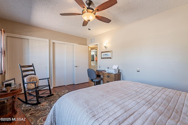 bedroom with visible vents, ceiling fan, multiple closets, wood finished floors, and a textured ceiling