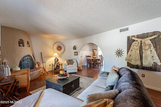 living room featuring visible vents, a fireplace, arched walkways, a textured ceiling, and wood-type flooring