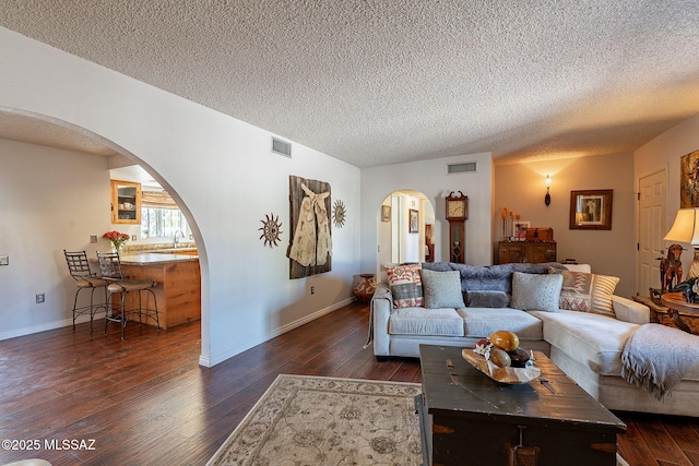 living room with dark wood-type flooring, visible vents, arched walkways, and a textured ceiling