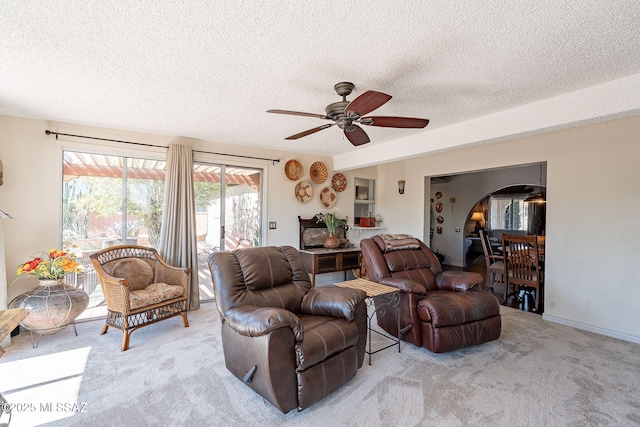 living area with arched walkways, a textured ceiling, light carpet, and ceiling fan