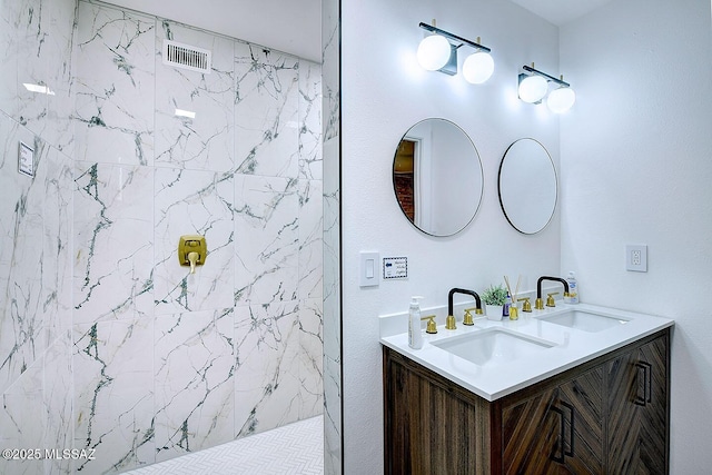 bathroom featuring double vanity, a tile shower, and a sink