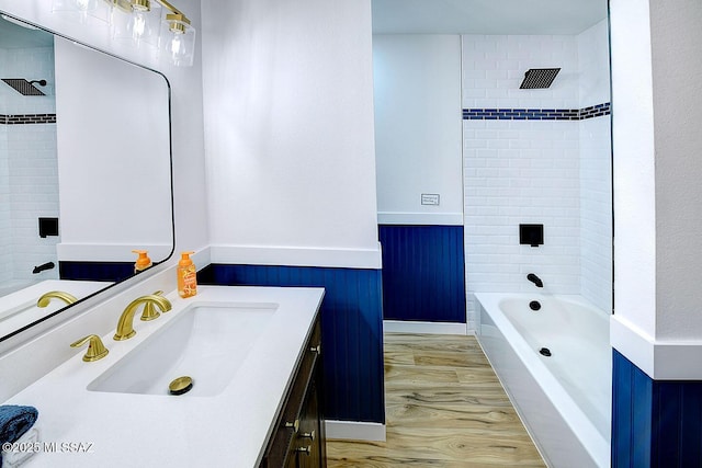 bathroom with visible vents, wainscoting, shower / bathing tub combination, wood finished floors, and vanity