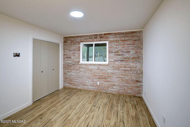 unfurnished bedroom with a closet, baseboards, wood finished floors, and brick wall