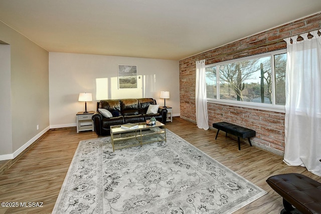 living area featuring brick wall, baseboards, and wood finished floors